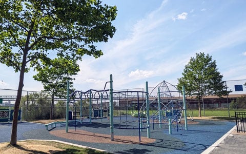 A playground with various climbing structures and play equipment is set on a soft, blue safety surface. 
