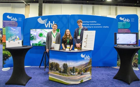  Alex Shulz, Kelsey Munns, and Connor Mountain stand in front of a display at a conference.