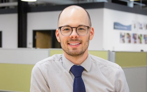 Donny Goris-Kolb in glasses and a button down shirt, leaning on a desk.