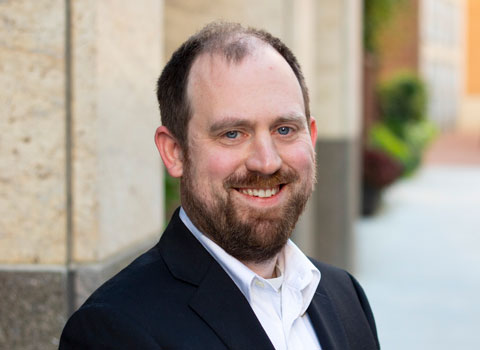 Professional headshot of Michael Lowder wearing business casual attire while smiling outside. 