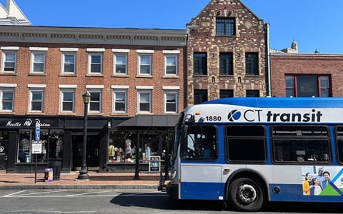 A blue-and-white CTtransit bus at a bus stop in front of a brick building.