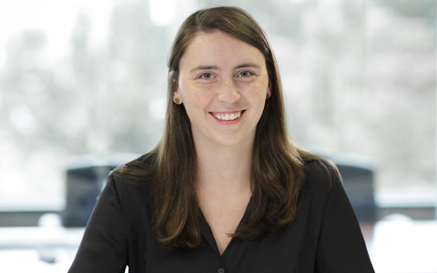Noelle Rauer sits at her desk and smiles at the camera wearing a black shirt.