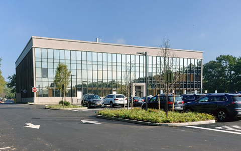 Parking lot with trees and a windowed building against a blue sky.