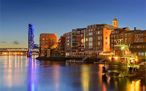 Tugboats on the water at sunset with brick buildings and bridge.