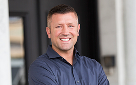 Justin Dufresne smiling with arms crossed, standing in front of a building with columns.