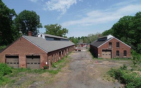 Two vacant industrial buildings surrounded by woods.