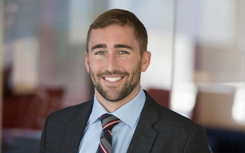 Seth Lattrell posing in the office with a suit and tie.