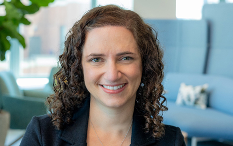 A smiling woman with curly brown hair in a black blazer.
