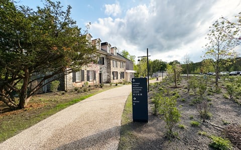 Pathway to building surrounded by greenery and a directional sign.