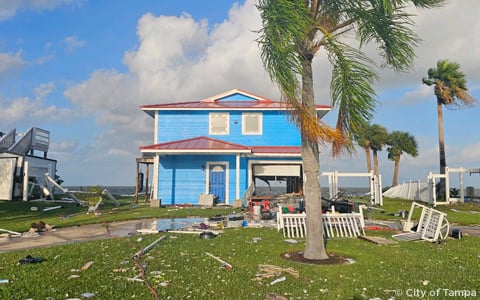 A blue beach house with storm damage on the coast.