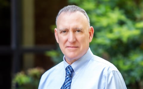 Tim Bryant stands outside in a blue shirt and tie.