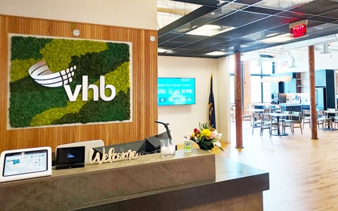 VHB logo on moss sign mounted over reception desk, adjacent to café area with bright windows.