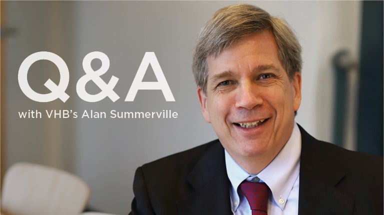 Alan Summerville smiles at the camera in black coat and red tie.