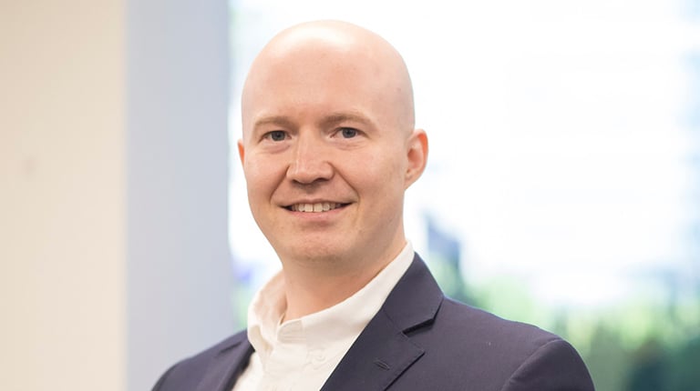 Andrew Buck smiling in a white shirt and blue blazer.