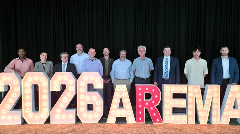 A group photo of 11 VHB team members standing behind a large floor sign that reads 2026 AREMA. 