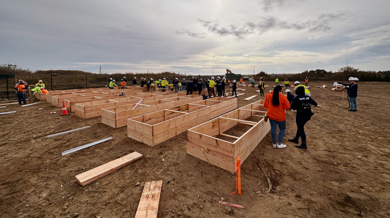 Group of people in a field with wooden planter beds.