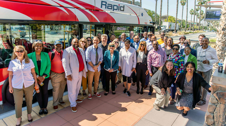 A group of people stand outside a rapid transit bus on a San Diego street.