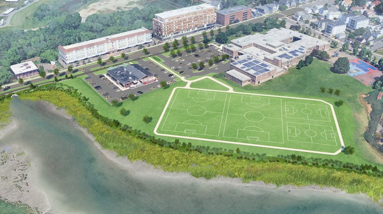 Aerial view of a green sports complex featuring multiple soccer fields with marked goals. Surrounding the fields is a pathway. 
