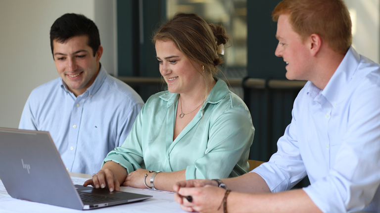 Drew Dommel, Aimee Barnes, and Matt Bruno gather together around a laptop in office.