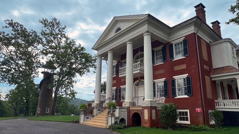 Historic red brick mansion with white columns and black shutters, viewed from the front drive.
