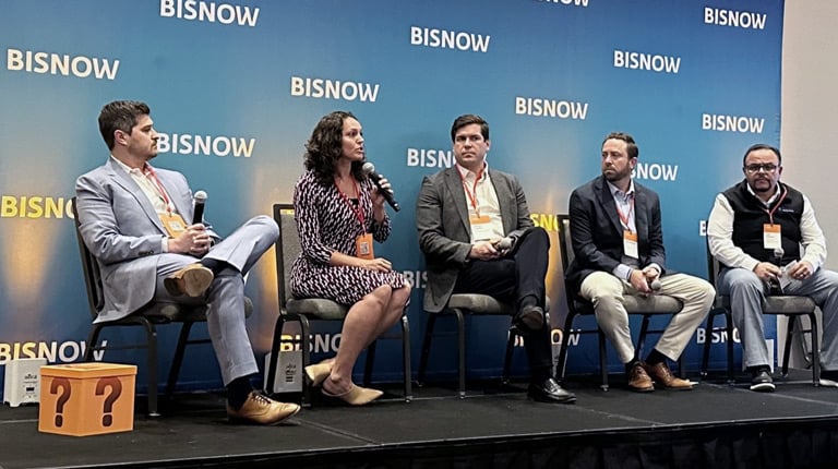A panel of five individuals seated on stage in front of a "Bisnow" backdrop, engaging in discussion. 