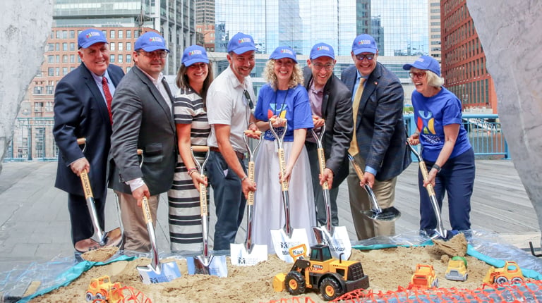 A group of individuals in business attire and blue caps are participating in a groundbreaking ceremony.  