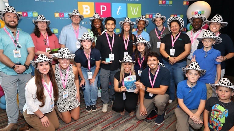 A group of coworkers stand in front of a Best Places to Work banner.