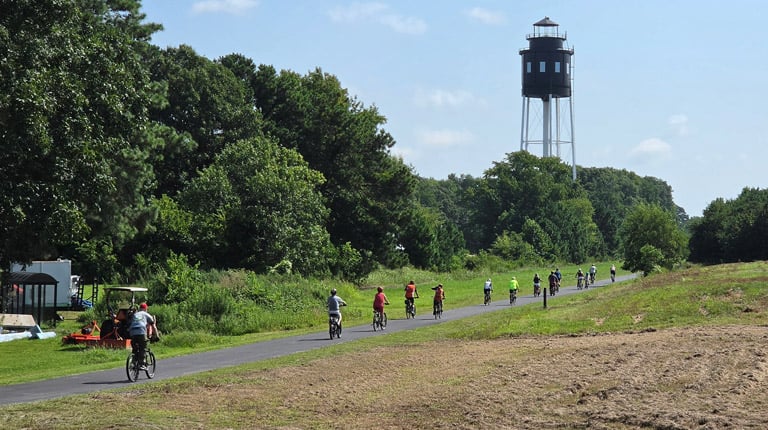 Bicycle riders on a rural bike path with a water tower in sight.
