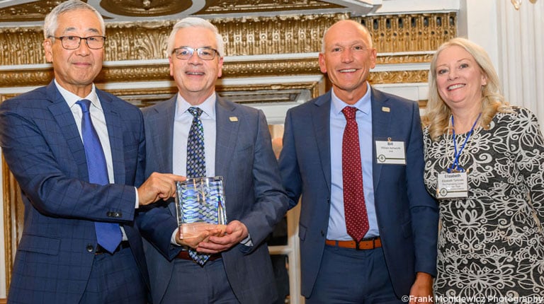 Four individuals smiling at the camera holding an award.