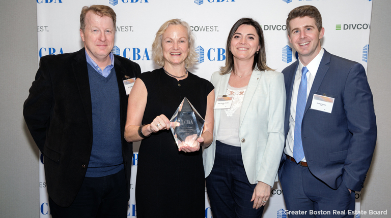 Four people stand with an award in front of a white banner.