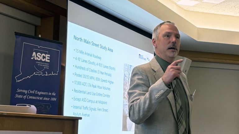 A person is speaking at a podium in a conference room. Behind them, a presentation slide displays text titled "North Main Street Study Area."