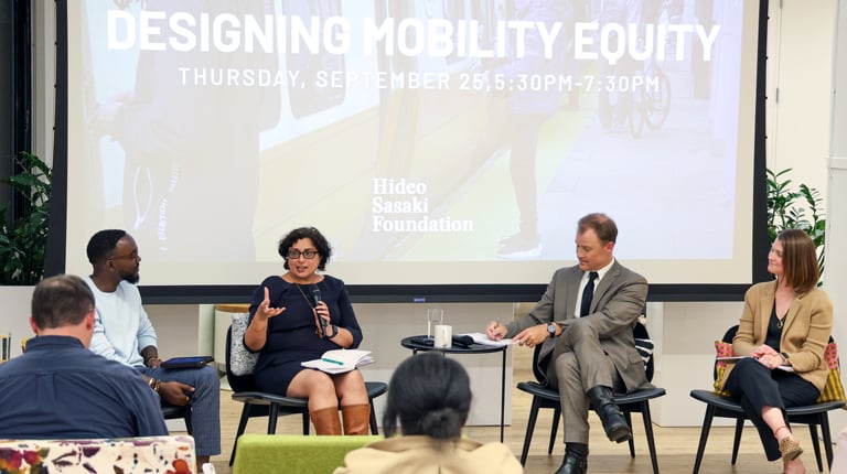 A modern conference room hosts a panel discussion on 'Designing Mobility Equity,' organized by the Hideo Sasaki Foundation. Audience members sit on colorful and contemporary furniture, attentively listening to the speakers.