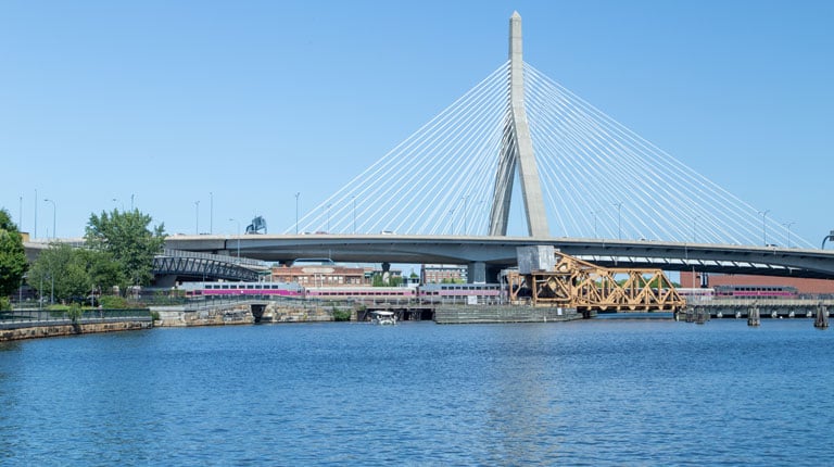 A train crossing a draw bridge, beneath a suspension bridge