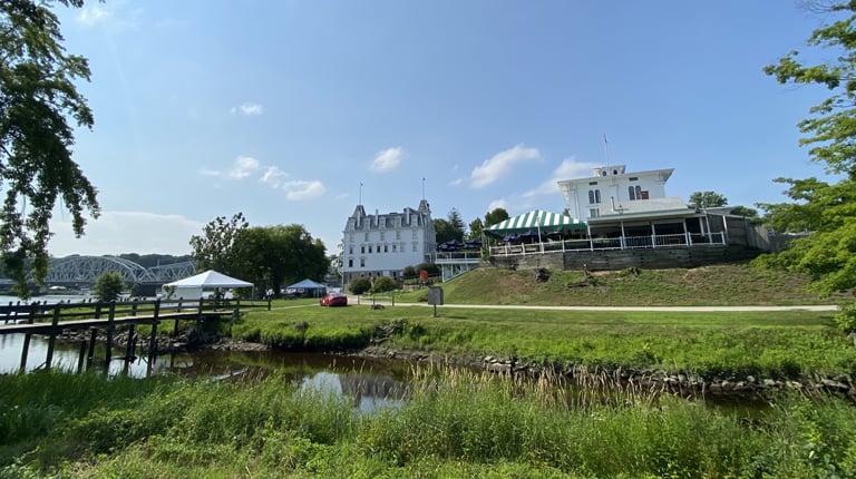 View of a serene river landscape with distinctive white buildings and green trees under a clear blue sky.