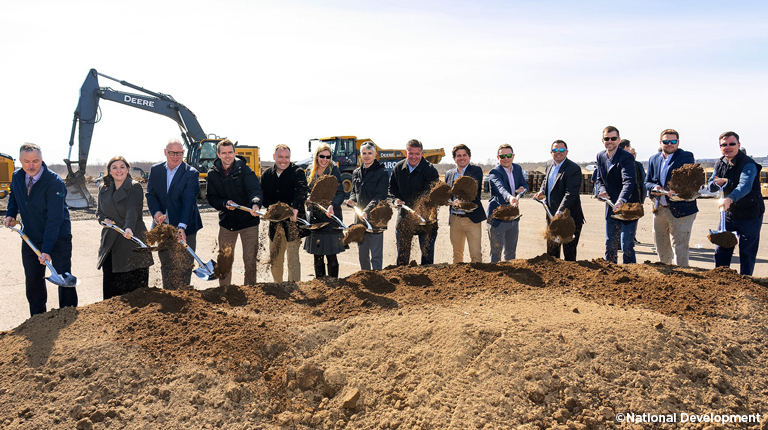 Men and women stand with shovels in their hands during a groundbreaking ceremony.