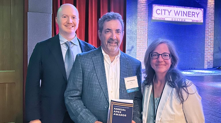 Three individuals stand on stage at City Winery, smiling with one person holding an 'EBC Annual Awards' program.