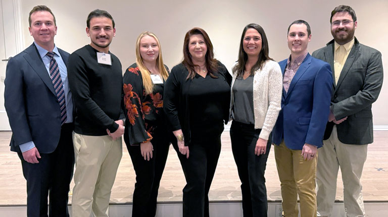 Seven people smiling and standing together, facing the camera.