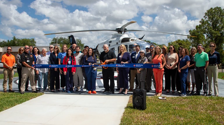 The project team smiling and getting ready to cut the ribbon on the new helipad in front of a helicopter. 
