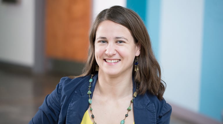 A woman with long brown hair wearing a blue jacket and turquoise necklace