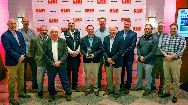 Group of people posing with an award in front of an "ENR" branded backdrop. The individuals are standing together, and one is holding a trophy. 