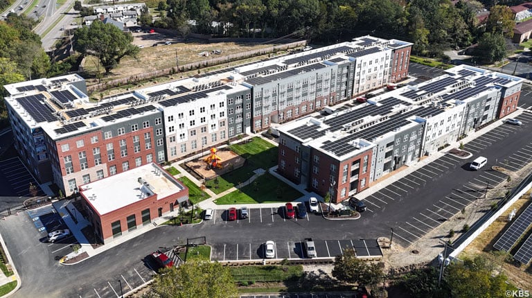 Aerial shots of an affordable multifamily housing project featuring solar panels, a playground, parking, and green spaces for residents.