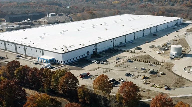 White industrial building with parking surrounded by trees.