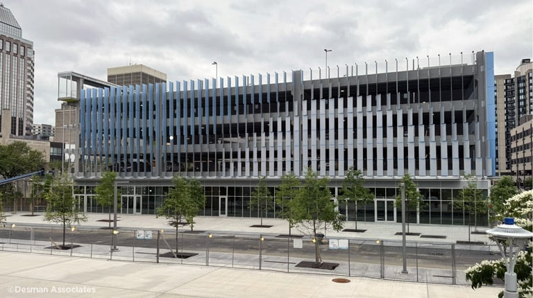 A modern multi-story parking garage with a sleek, blue and gray exterior is seen on a cloudy day.