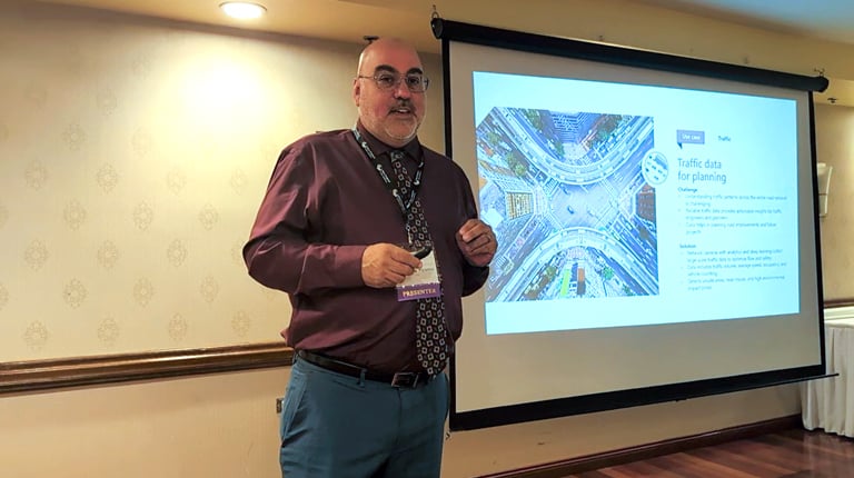 A person standing in a room gives a presentation next to a projected slide titled "Traffic data for planning" by Waze. 