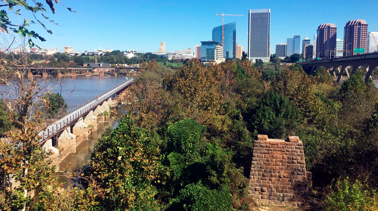Pedestrian bridge across the James River with the skyline in the background.