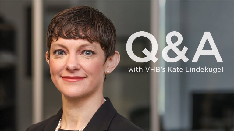 Kate Lindekugel in the office, wearing a dark suit and smiling. 