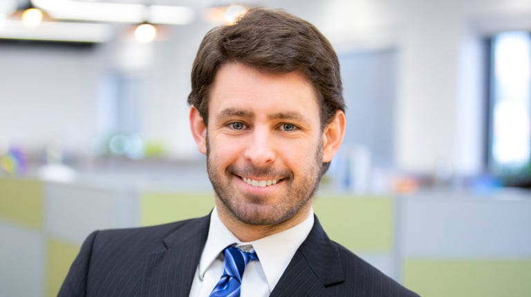 Ken Donald smiles in the office, wearing a blue striped tie and dark suit.