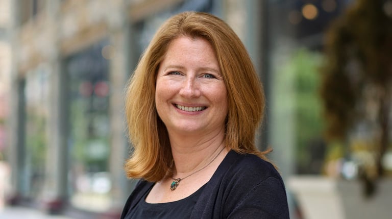 Lee Farmer in a black dress on a city sidewalk in the daytime with buildings in the background.