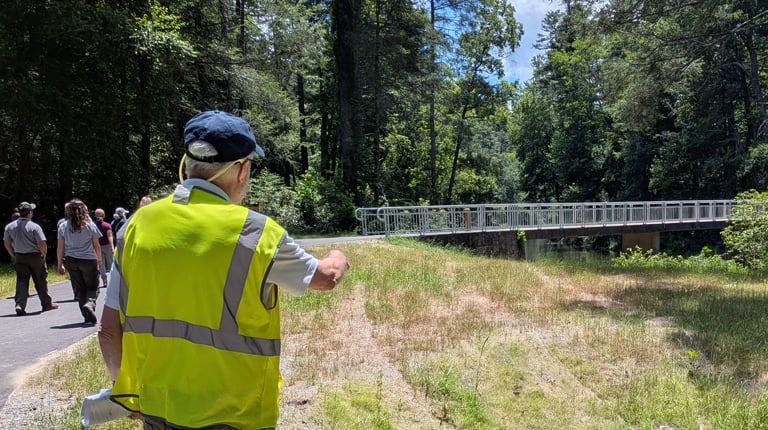 Doug Mettler wearing a yellow high visibility vest pointing at a storm drain while on a site visit.