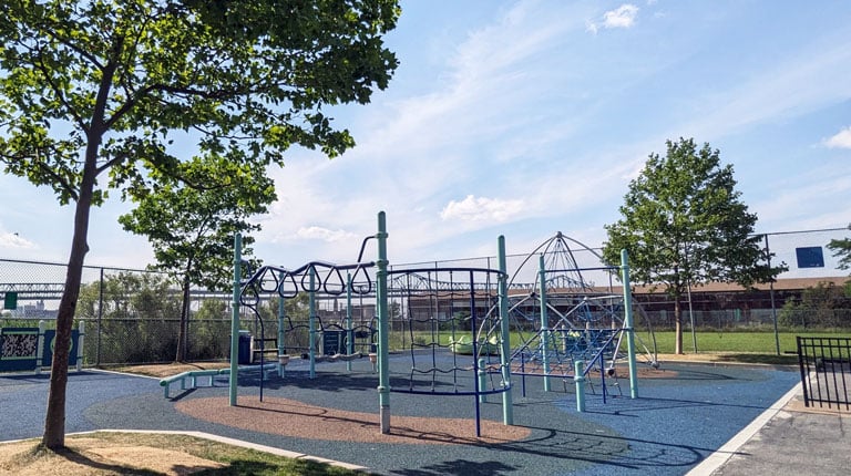 A playground with various climbing structures and play equipment is set on a soft, blue safety surface. 